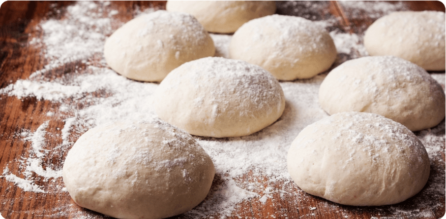 Flour-dusted pizza dough balls on a wooden table